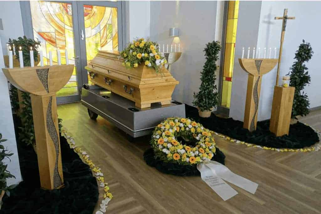 Sargdekoration mit einem Sargschmuck, Blütenkranz mit Schleife und Blütenblätter